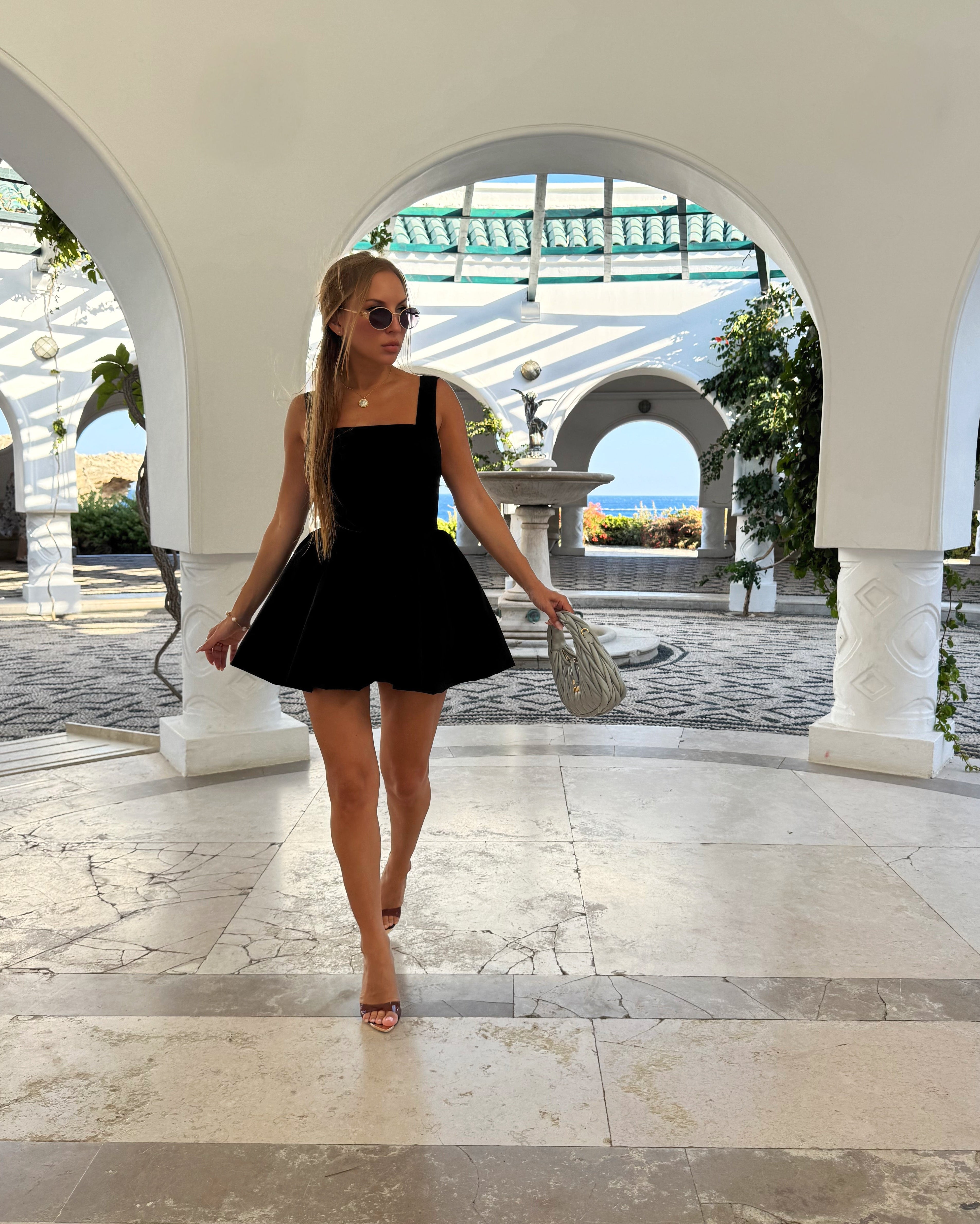 Woman in a black dress walking through an arched entrance with a scenic background