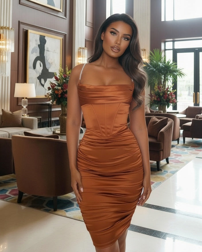 Woman in a brown dress standing in an elegant interior setting with chandeliers and artwork.