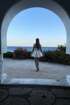 Woman in a white dress standing in front of an archway with a scenic view of the ocean.