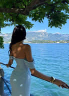 Woman in a light blue dress standing by a railing overlooking a lake with mountains in the background