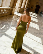 Woman in a green dress standing in a sunlit hallway with marble floors and columns.