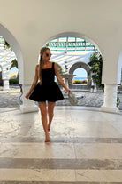 Woman in a black dress walking through an arched entrance with a scenic background