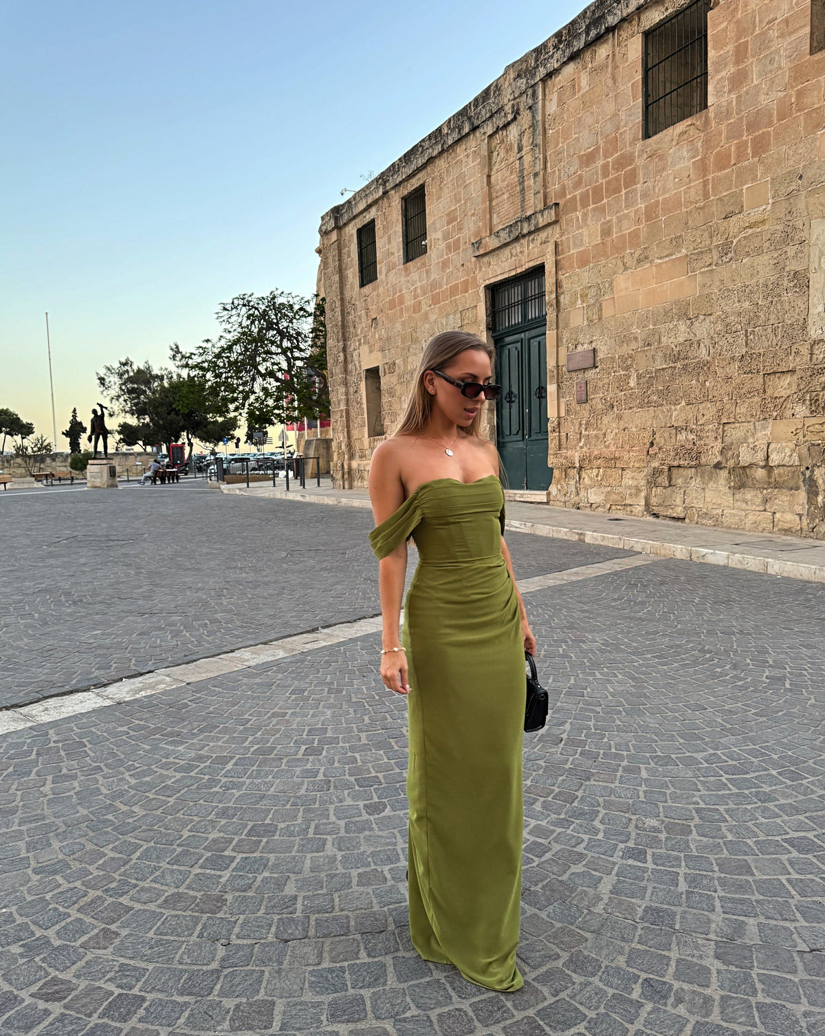 Olive green off-shoulder maxi dress worn on cobblestone street - DE NOIR Charlotte